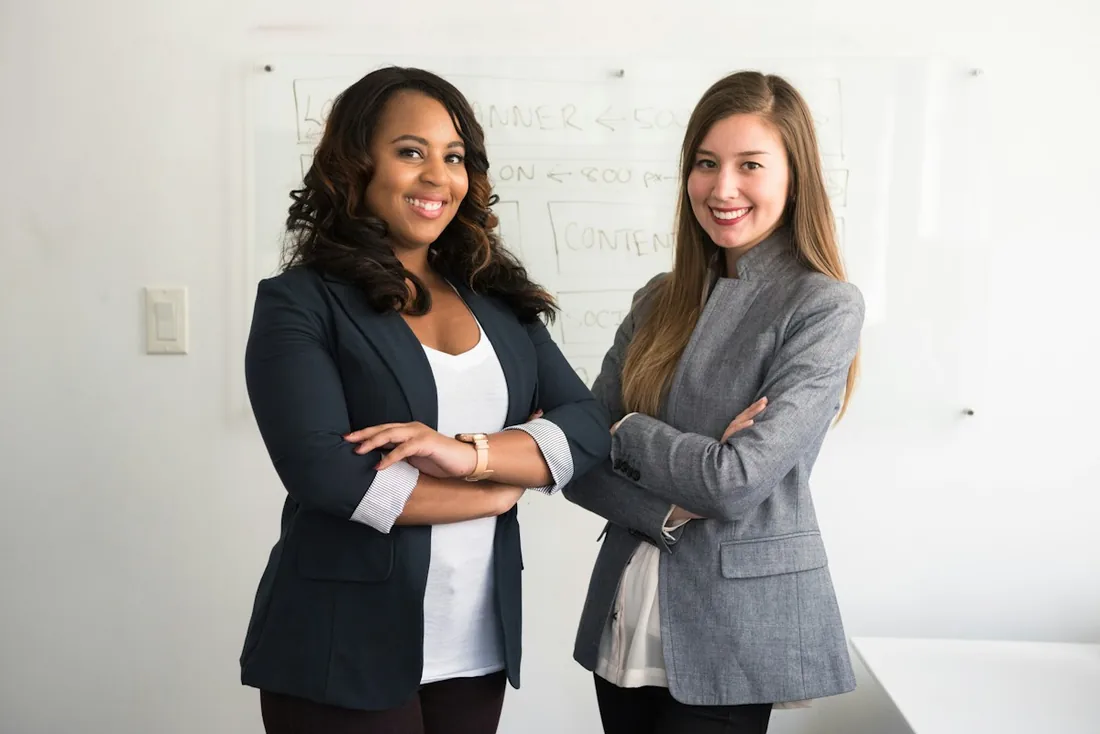 Deux professionnelles devant un tableau blanc dans un bureau.