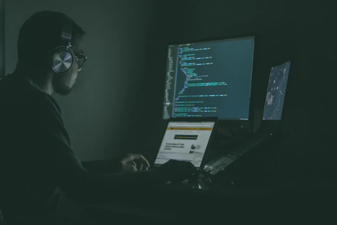 Professionnel devant plusieurs écrans affichant du code dans un espace sombre.