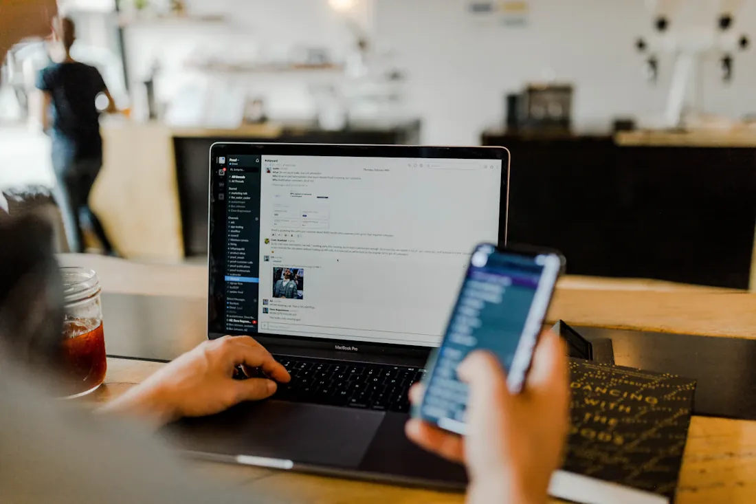 Personne consultant un smartphone devant un ordinateur portable.